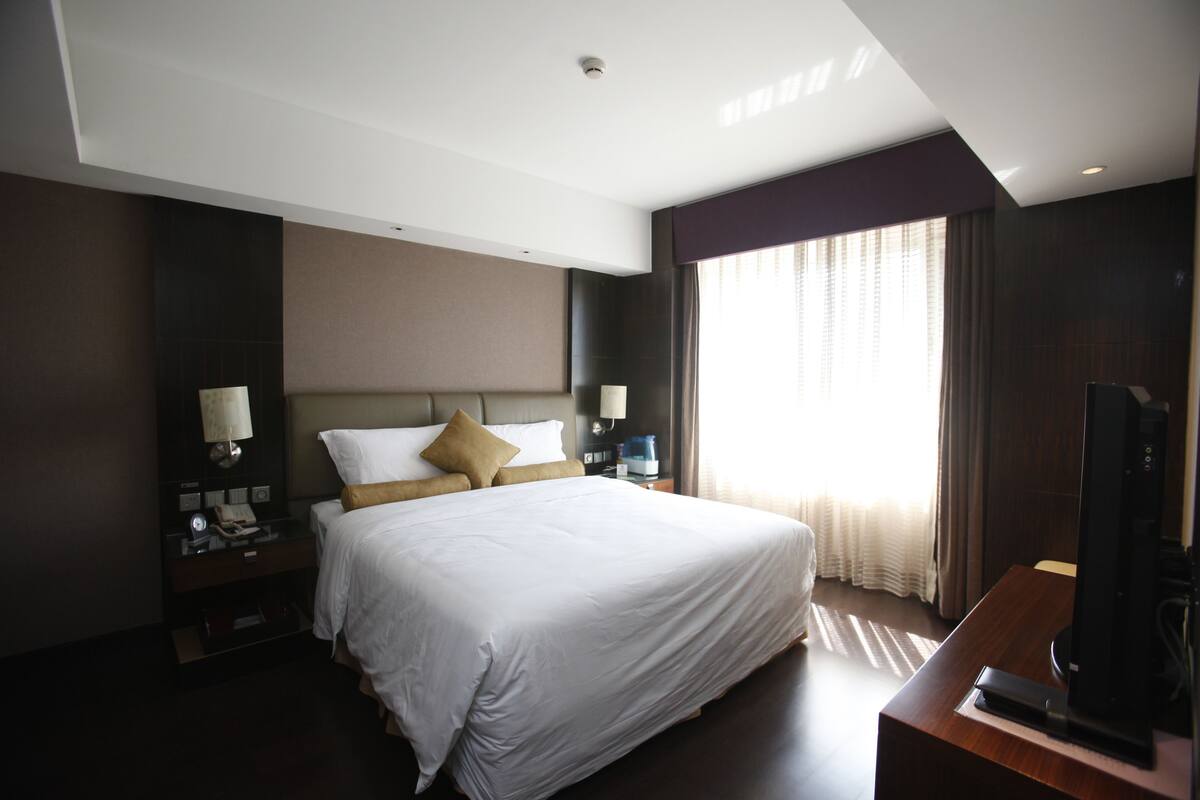 A hotel room with a large bed, a television, a nightstand, and a window with curtains.