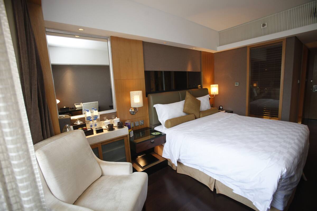 A hotel room with a large bed, a desk with a chair, a television, and a window with curtains.