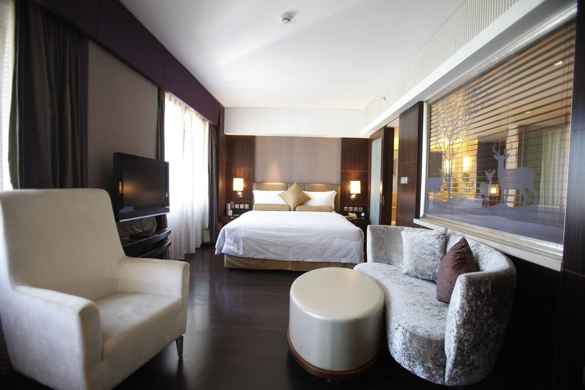 A hotel room with a bed, a TV, a sofa, and a chair.