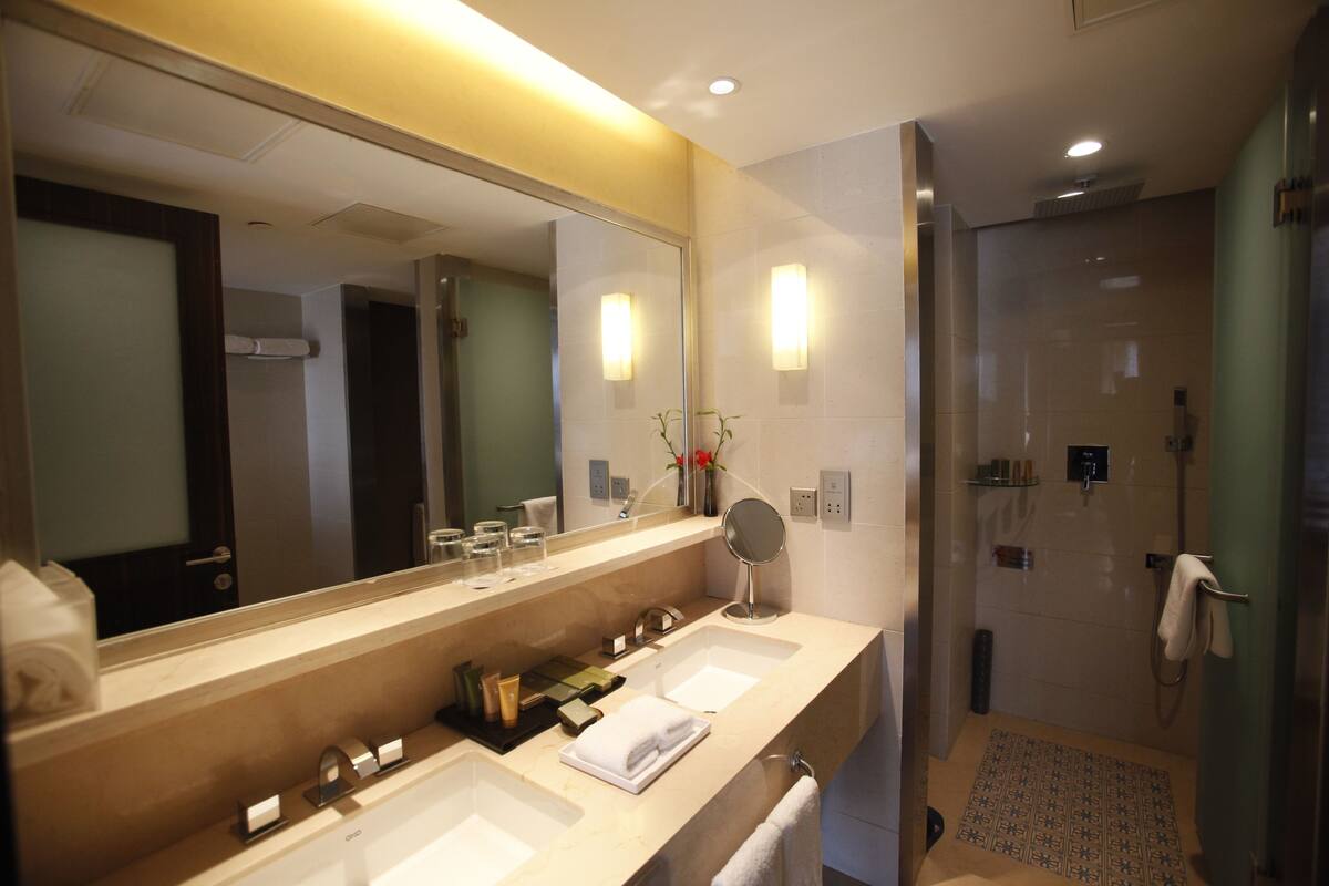 A modern bathroom with a large mirror, two sinks, a shower, and a towel rack.