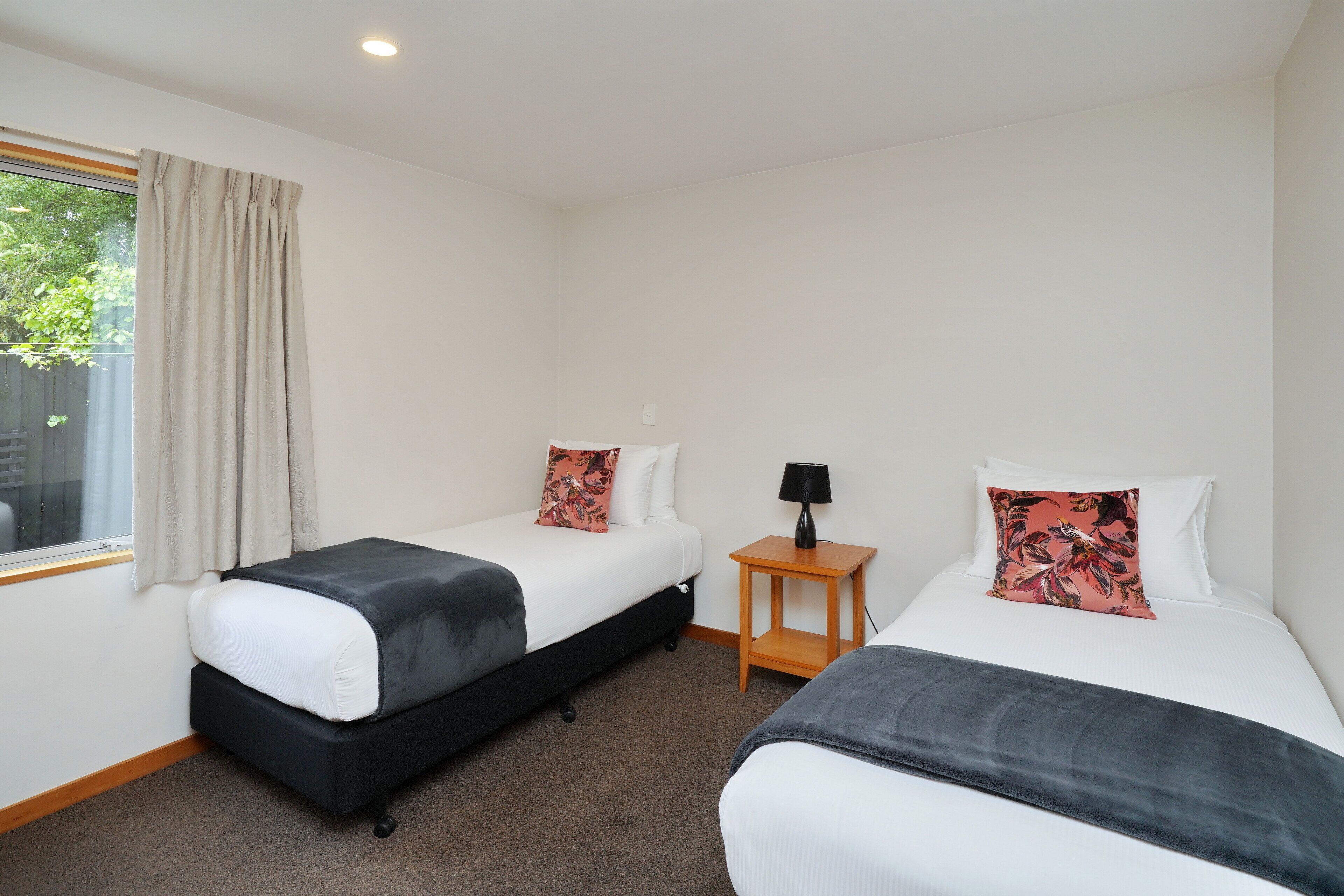 Una habitación de hotel con dos camas, una mesita con una lámpara y una ventana con cortinas.