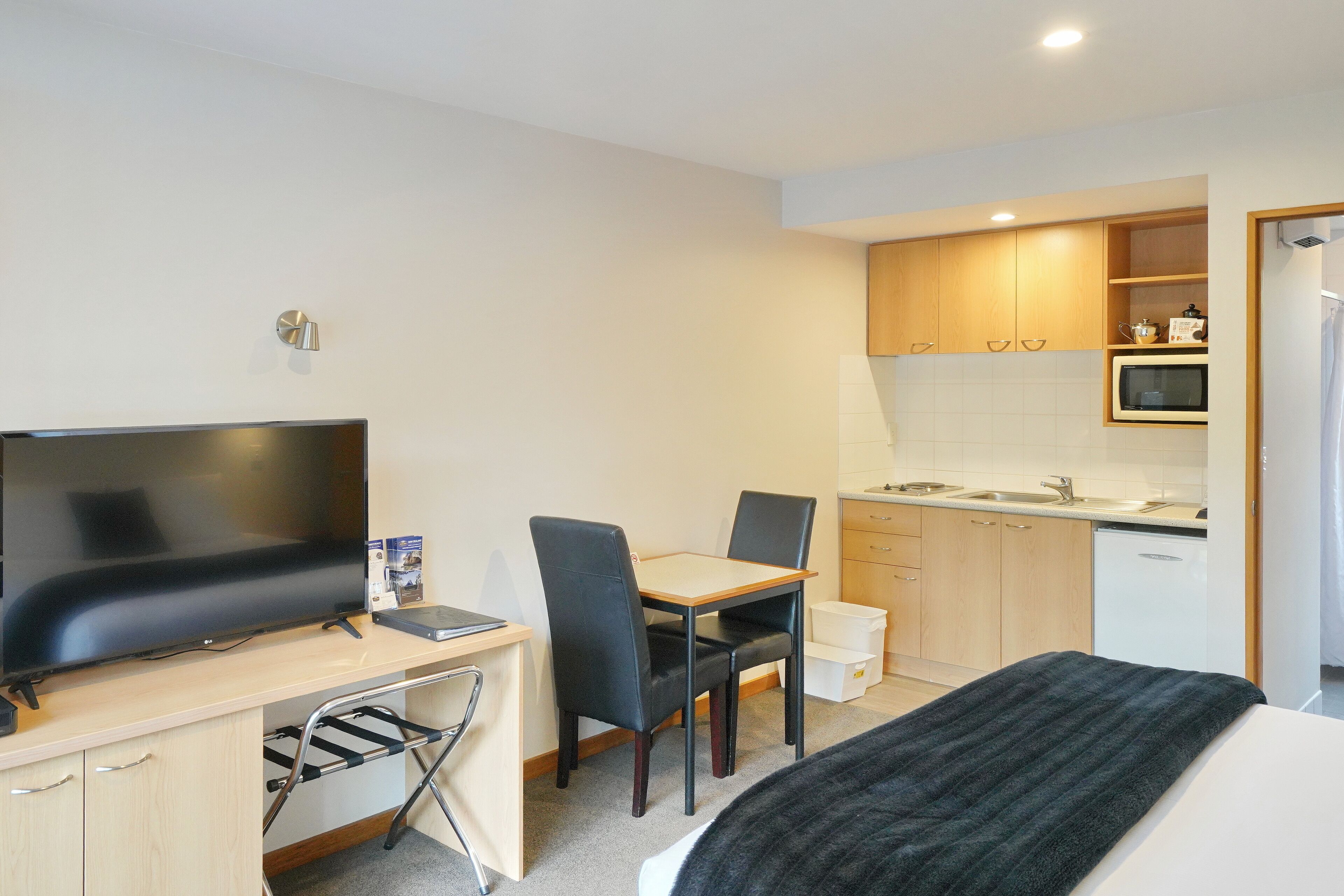 Ett kompakt hotellrum med en säng, ett skrivbord med en TV, en stol, ett litet bord, en mikrovågsugn och ett litet pentry.
