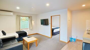 Habitación de hotel compacta con sofá, una pequeña mesa, televisor, dormitorio independiente con cama y kitchenette.