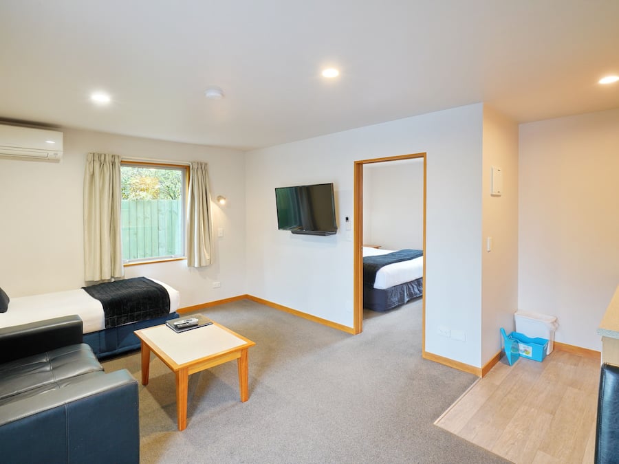 Habitación de hotel compacta con sofá, una pequeña mesa, televisor, dormitorio independiente con cama y kitchenette.