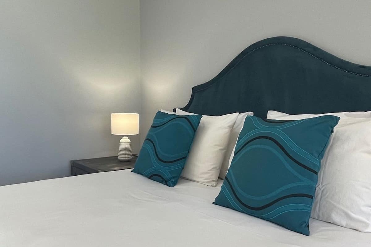 A neatly made bed with white bedding and teal pillows, a bedside lamp, and a nightstand.