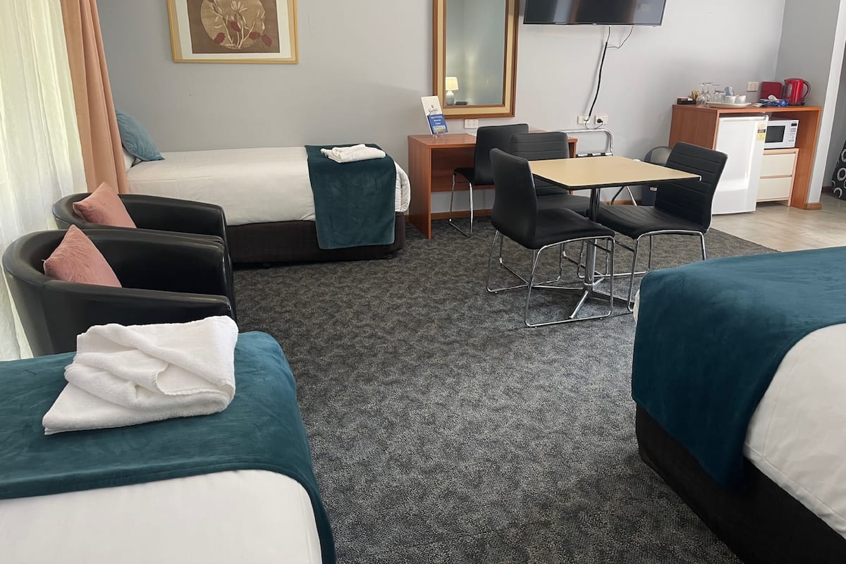 A hotel room with two beds, a desk with a chair, a television, a mirror, and a kitchenette.