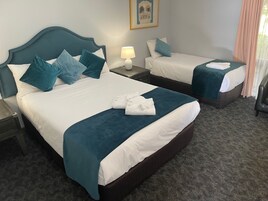 A hotel room with two beds, each with teal bedding and pillows, a nightstand with a lamp, and a framed picture on the wall.