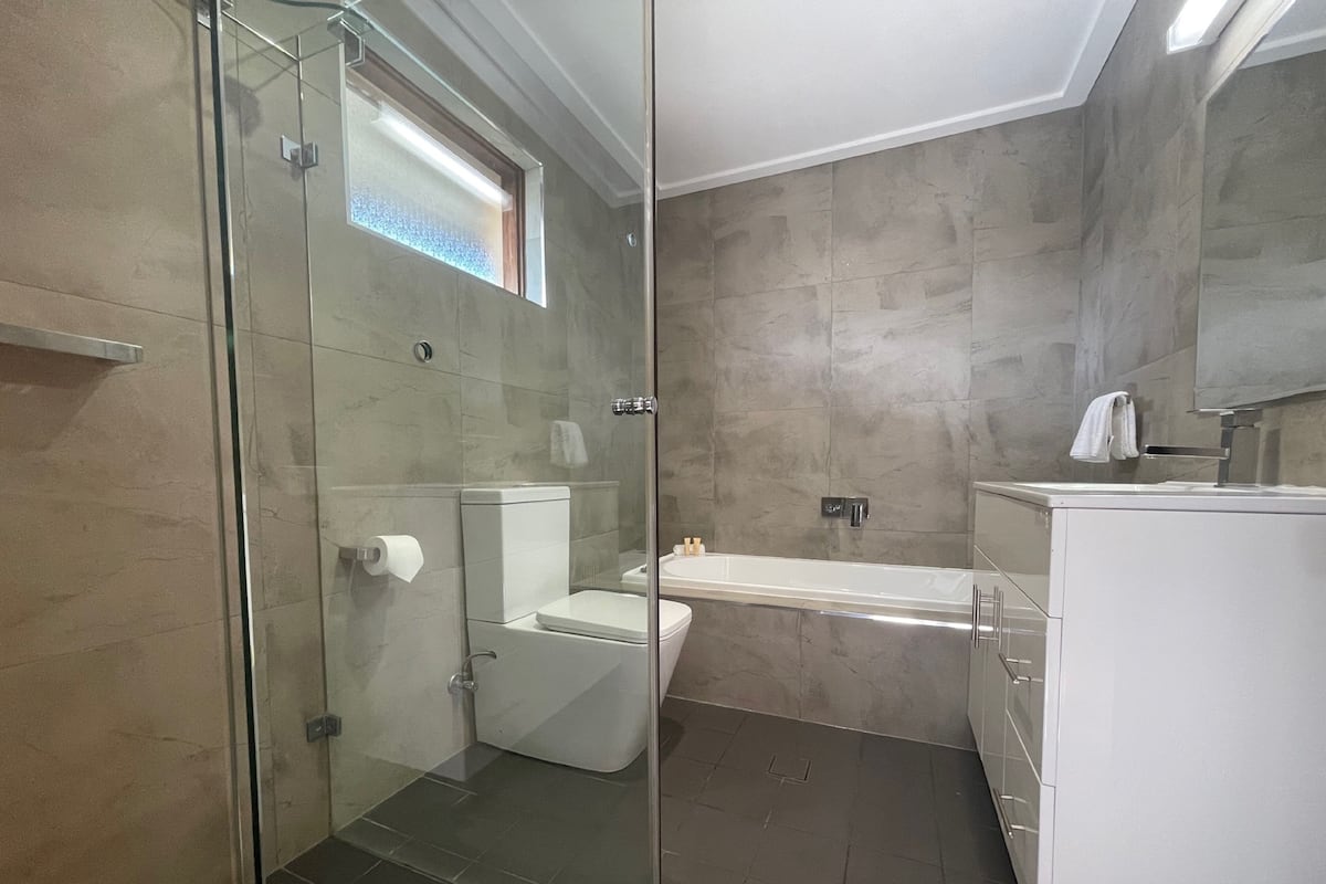A modern bathroom with a glass shower enclosure, a toilet, a bathtub, and a vanity with a mirror.