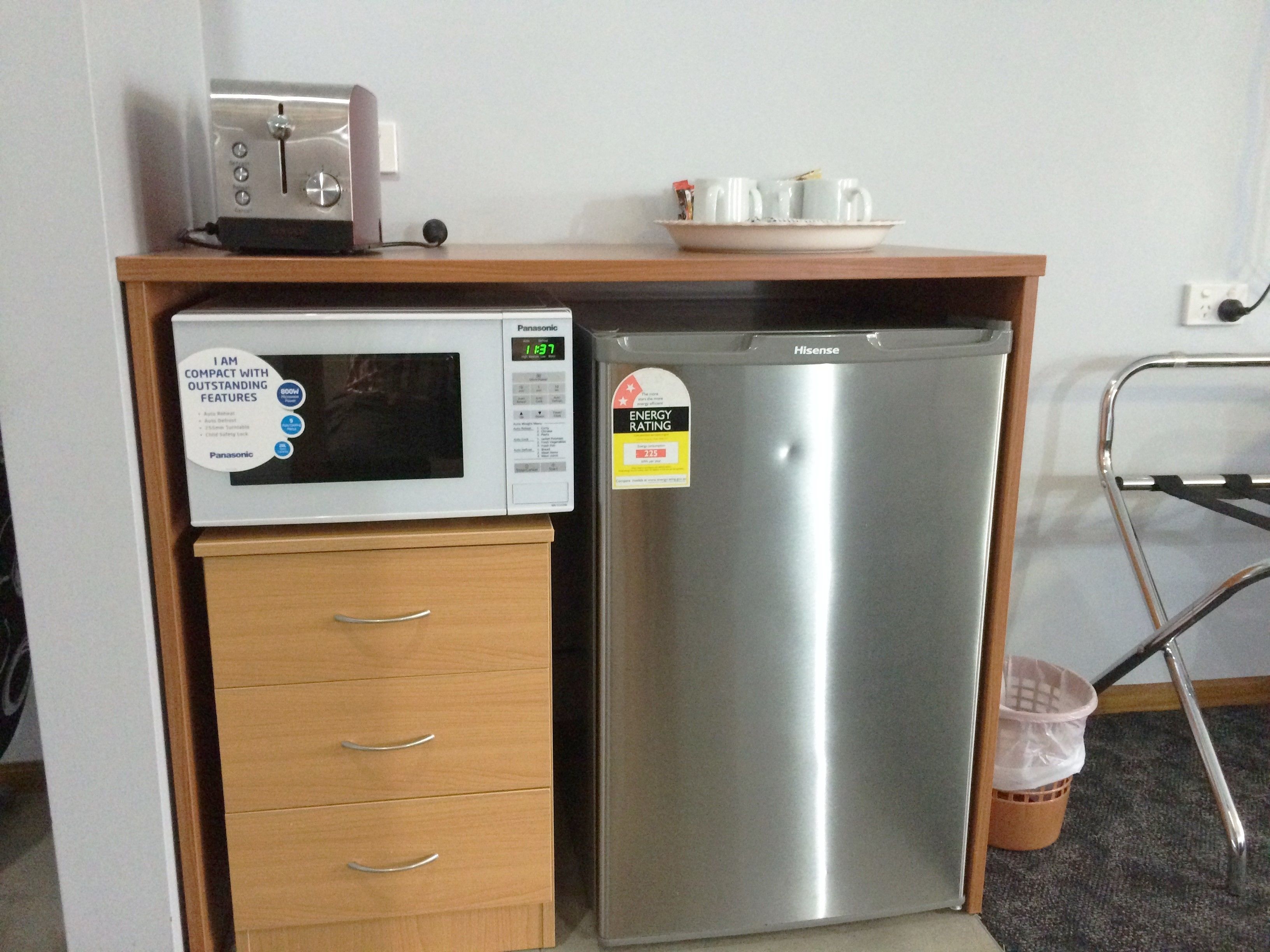 A compact kitchenette with a microwave, a Hisense refrigerator, and a wooden drawer unit.