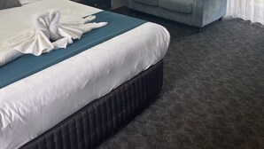 Une chambre d’hôtel avec un grand lit, un canapé gris, un tableau encadré au mur et une fenêtre avec des rideaux légers.