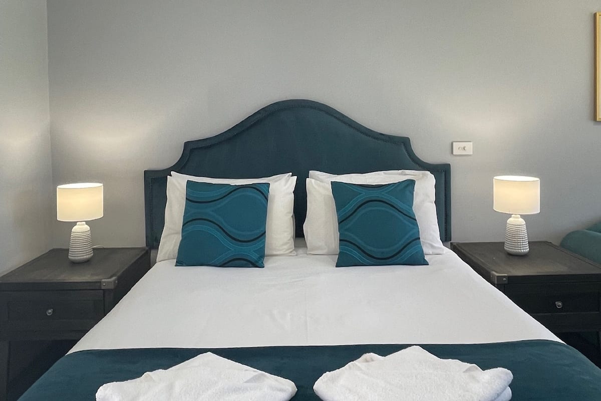A neatly made bed with white and teal bedding, two bedside lamps, and a headboard.