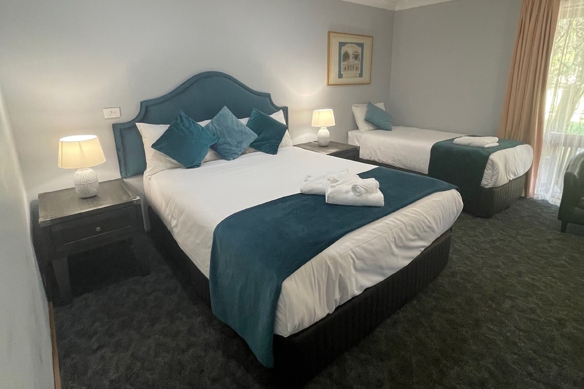 A hotel room with two beds, dark carpeting, and a ceiling light.