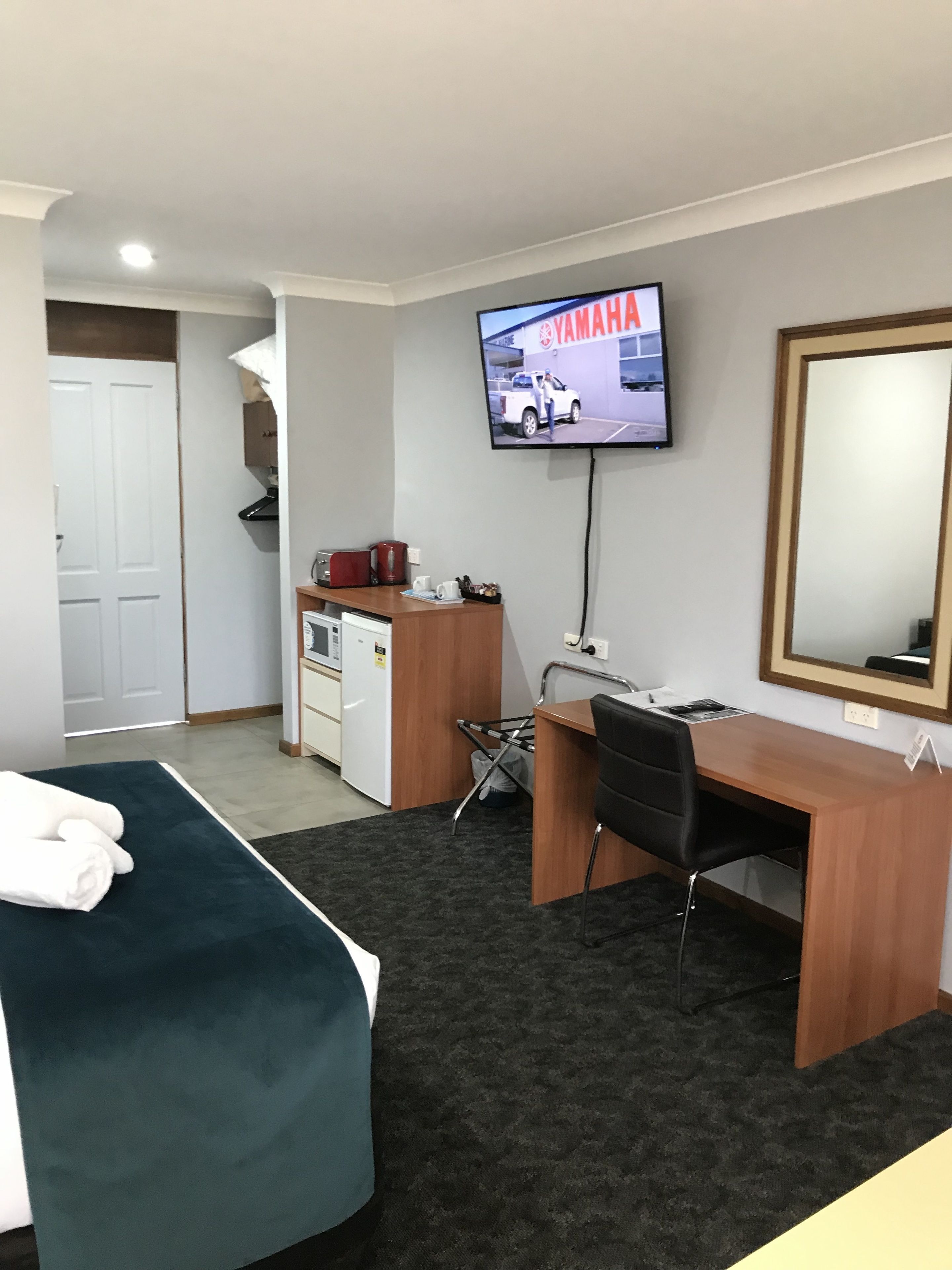 A hotel room with a bed, desk, chair, TV, and a small kitchenette.