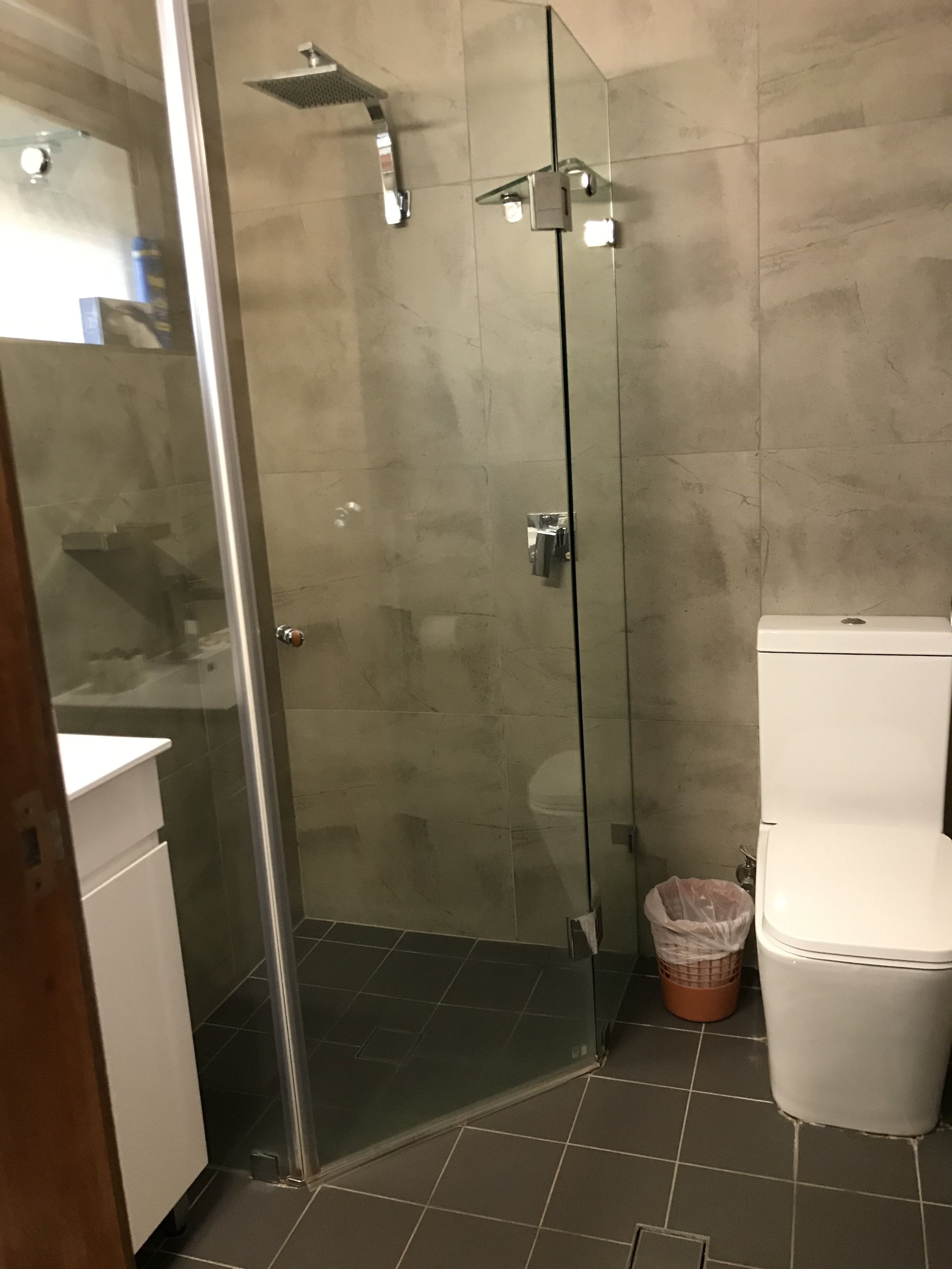 A modern bathroom with a glass-enclosed shower, a white toilet, and a trash bin.