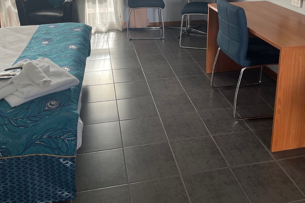 A hotel room with a bed, two chairs, a desk, and an air conditioning unit.
