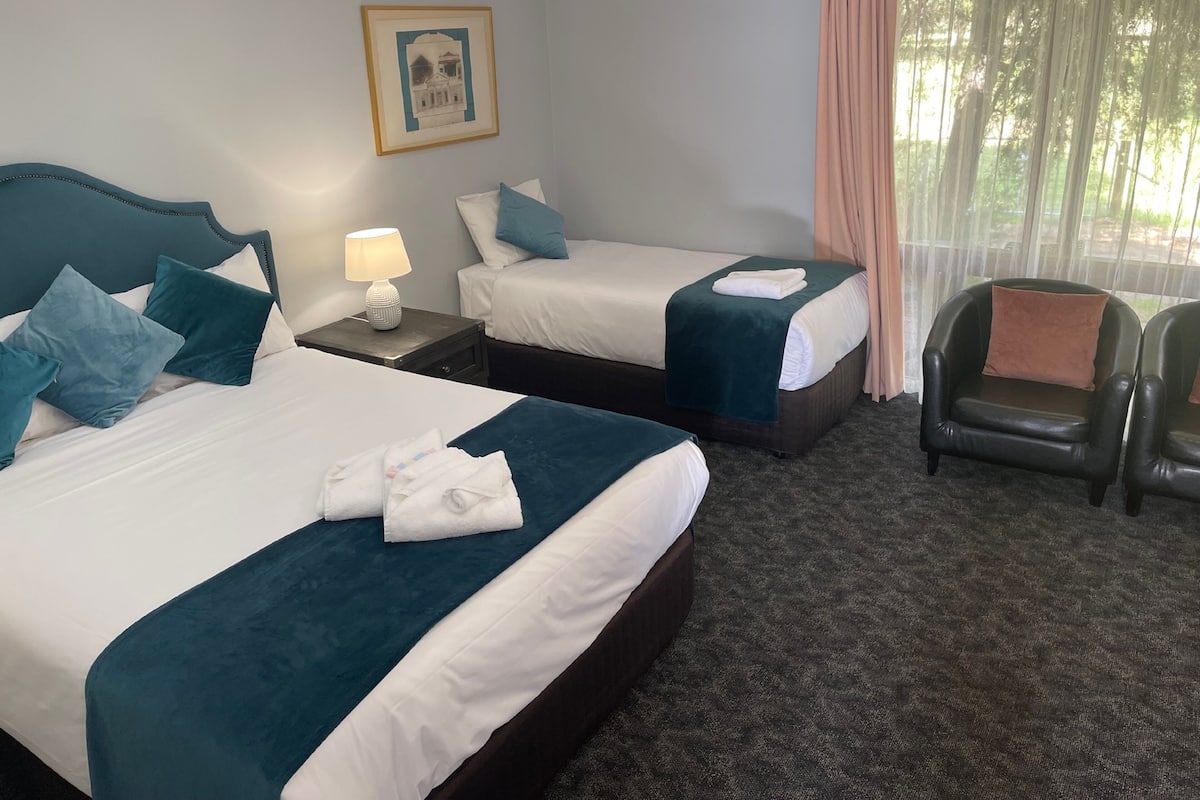 A hotel room with two beds, a nightstand with a lamp, a framed picture on the wall, and a chair.
