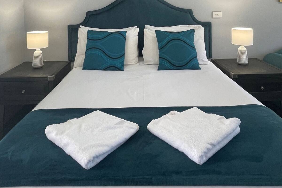 A neatly made bed with two pillows, two bedside tables with lamps, and a wall-mounted light fixture.