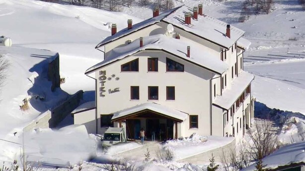Un hotel con fachada simétrica, múltiples chimeneas y un paisaje nevado con montañas al fondo.