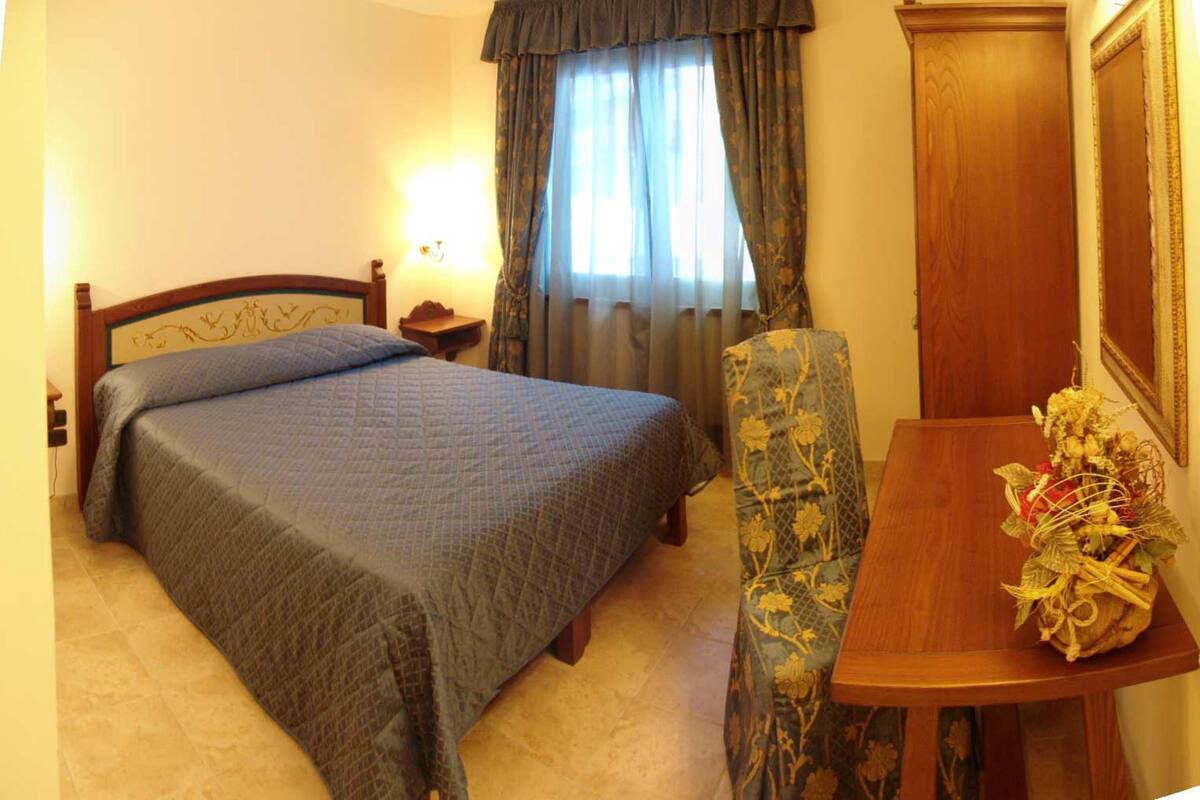 A hotel room with a bed, a chair, a table, and a mirror.