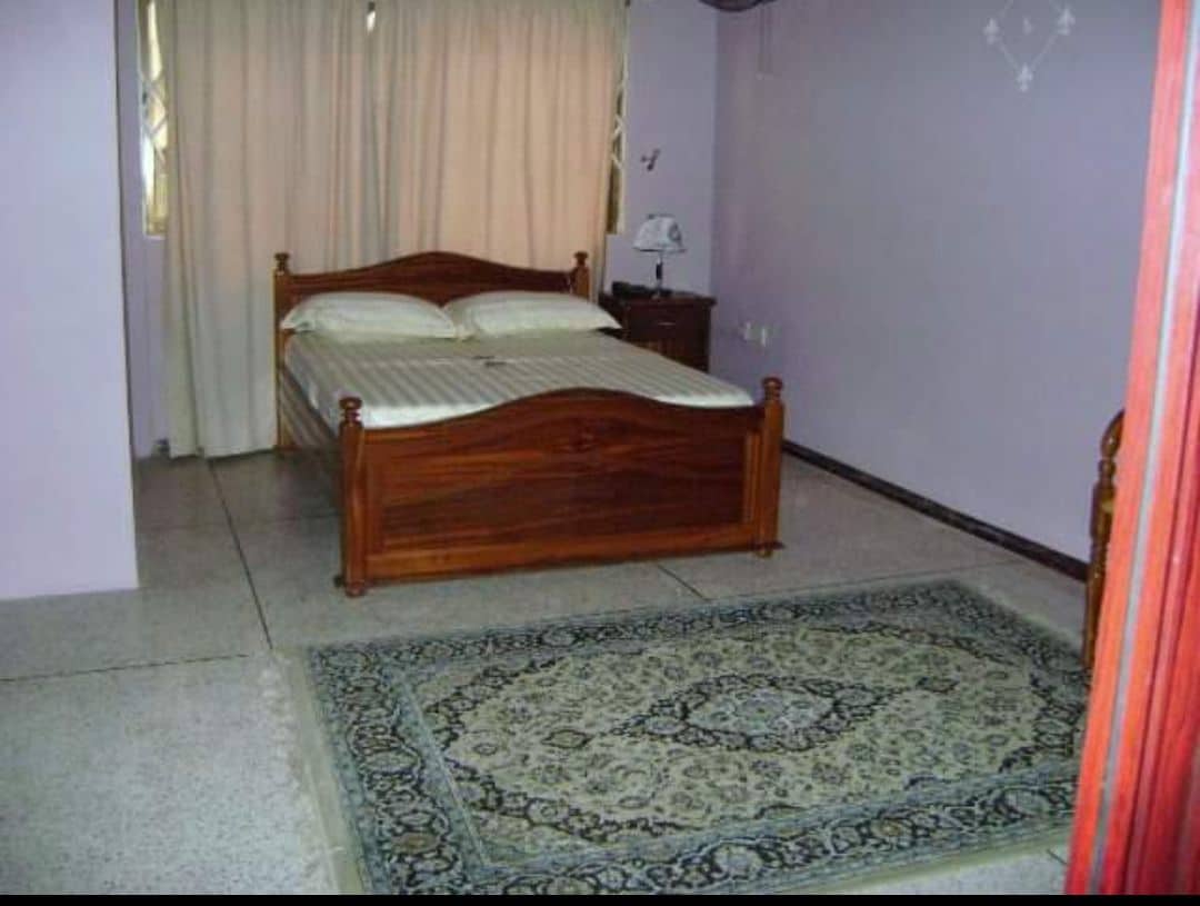 A bedroom with a wooden bed, a patterned rug, and a nightstand with a lamp.