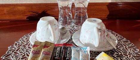 Una mesa con dos botellas de agua mineral, una cafetera, un hervidor de té y diferentes productos de café y té.