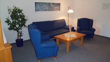 Ein Wohnzimmer mit einem blauen Sofa, einem Holztisch und einer Topfpflanze.