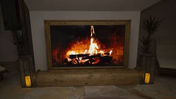 Una chimenea con fuego encendido, rodeada de suelo de piedra y repisas de madera.