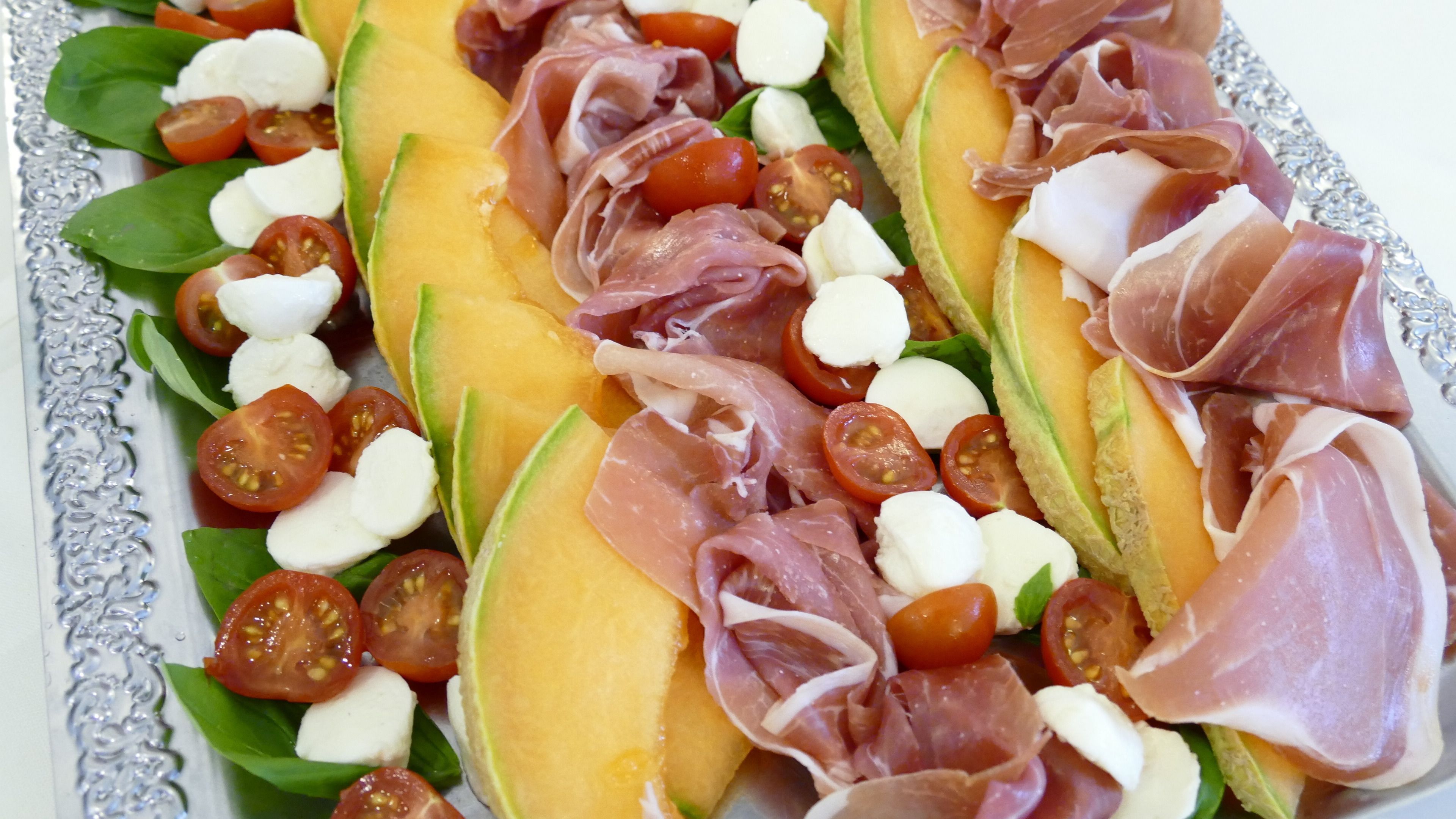 Een bord met meloen, tomaten, mozzarella en parmaham.