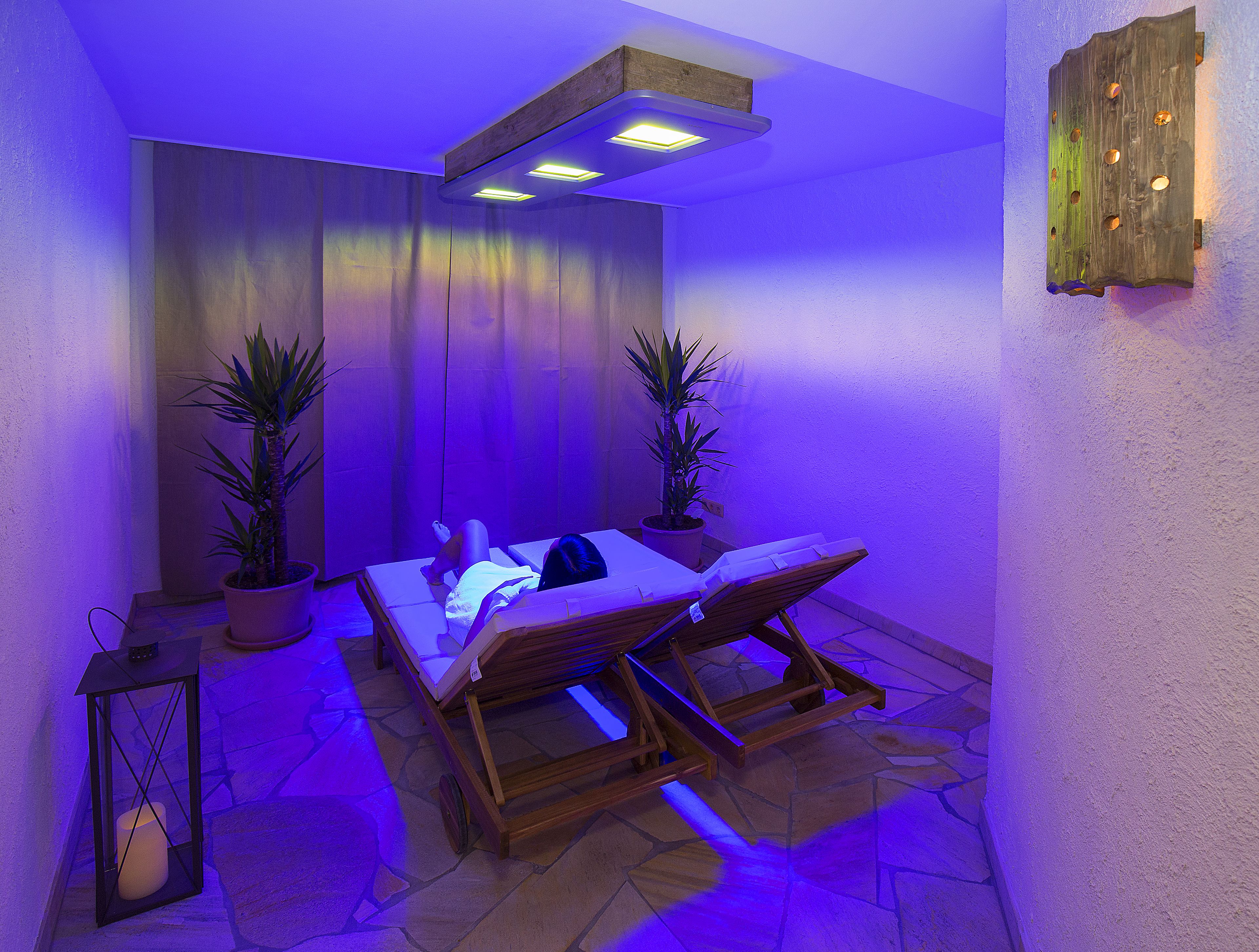 A spa room with a massage table, two potted plants, a wooden bench, and a stone floor.