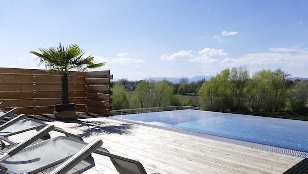 Una terraza de madera con piscina, sillas de descanso y una palmera.