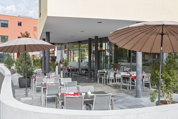 An outdoor cafe with tables and chairs, large umbrellas, and potted plants. - Villmergen Swiss Quality Hotel (Villmergen)