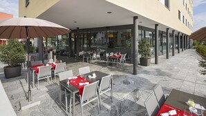 An outdoor dining area with tables and chairs, potted plants, and a covered section with a glass wall. - Villmergen Swiss Quality Hotel (Villmergen)