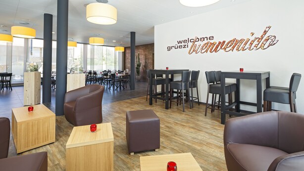 A modern hotel lobby with leather seating, wooden tables, and a large welcome sign. - Villmergen Swiss Quality Hotel (Villmergen)