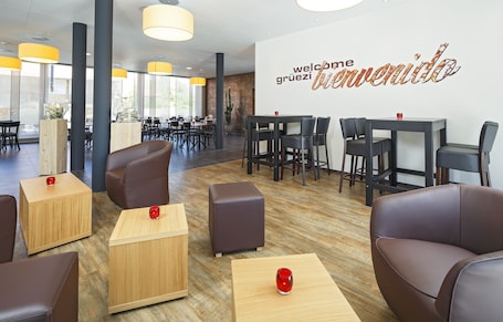 A modern hotel lobby with leather seating, wooden tables, and a large welcome sign.