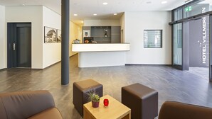 A modern hotel lobby with a reception desk, seating area, and a large pillar. - Villmergen Swiss Quality Hotel (Villmergen)