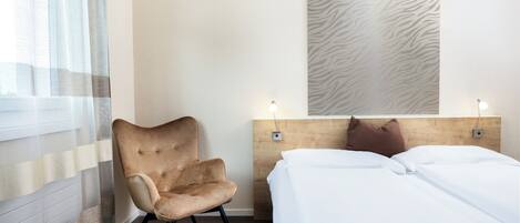 Habitación de hotel con cama, una silla, ventana con cortinas traslúcidas y pared con estampado de cebra.