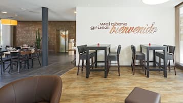 A modern interior with a 'welcome' sign, dining tables, chairs, and a wooden floor.