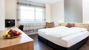 A hotel room with a bed, a desk with fruit, a chair, a TV, and a window with curtains. - Villmergen Swiss Quality Hotel (Villmergen)