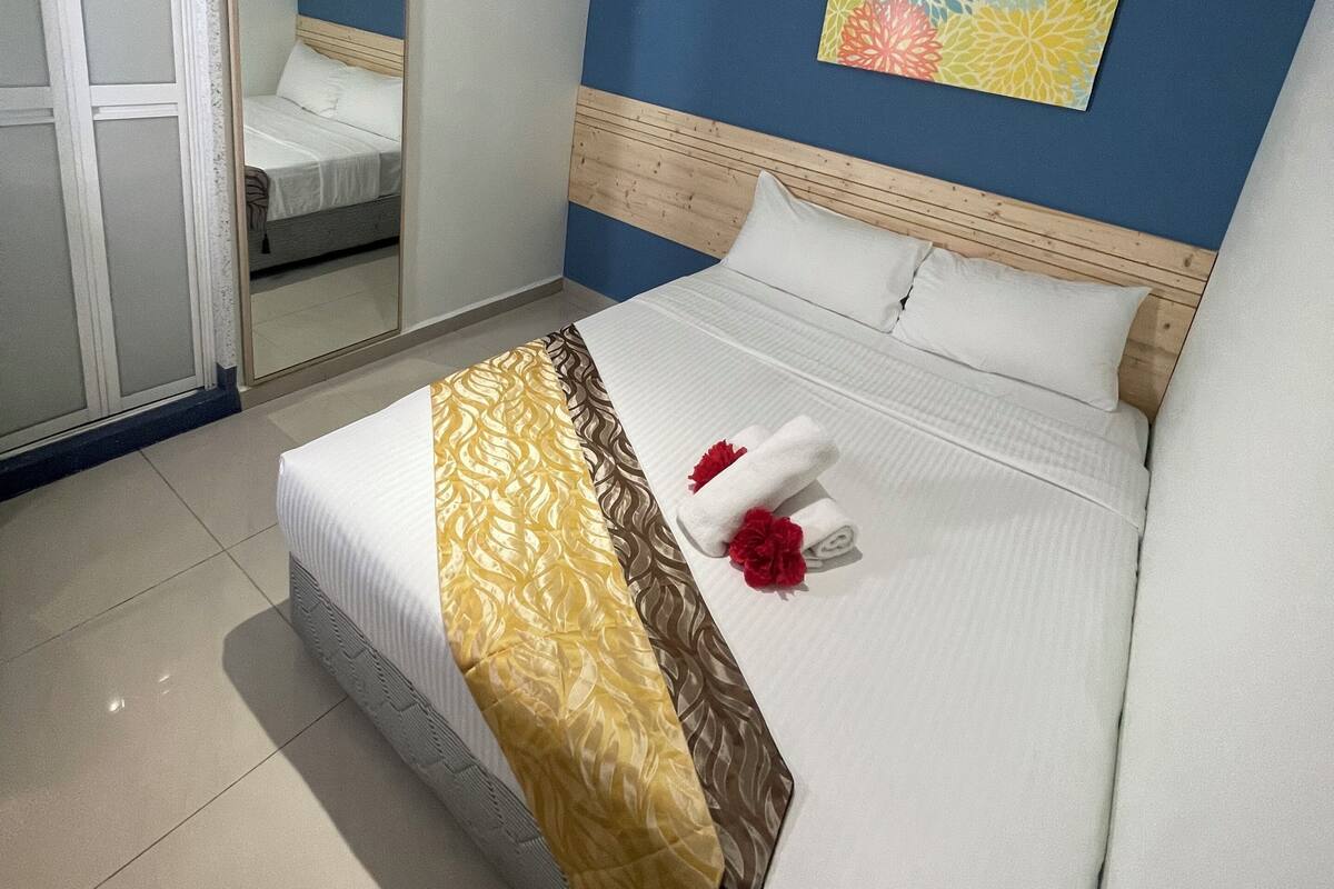 A neatly made bed with a patterned bedspread, a wooden headboard, and a wall-mounted mirror.