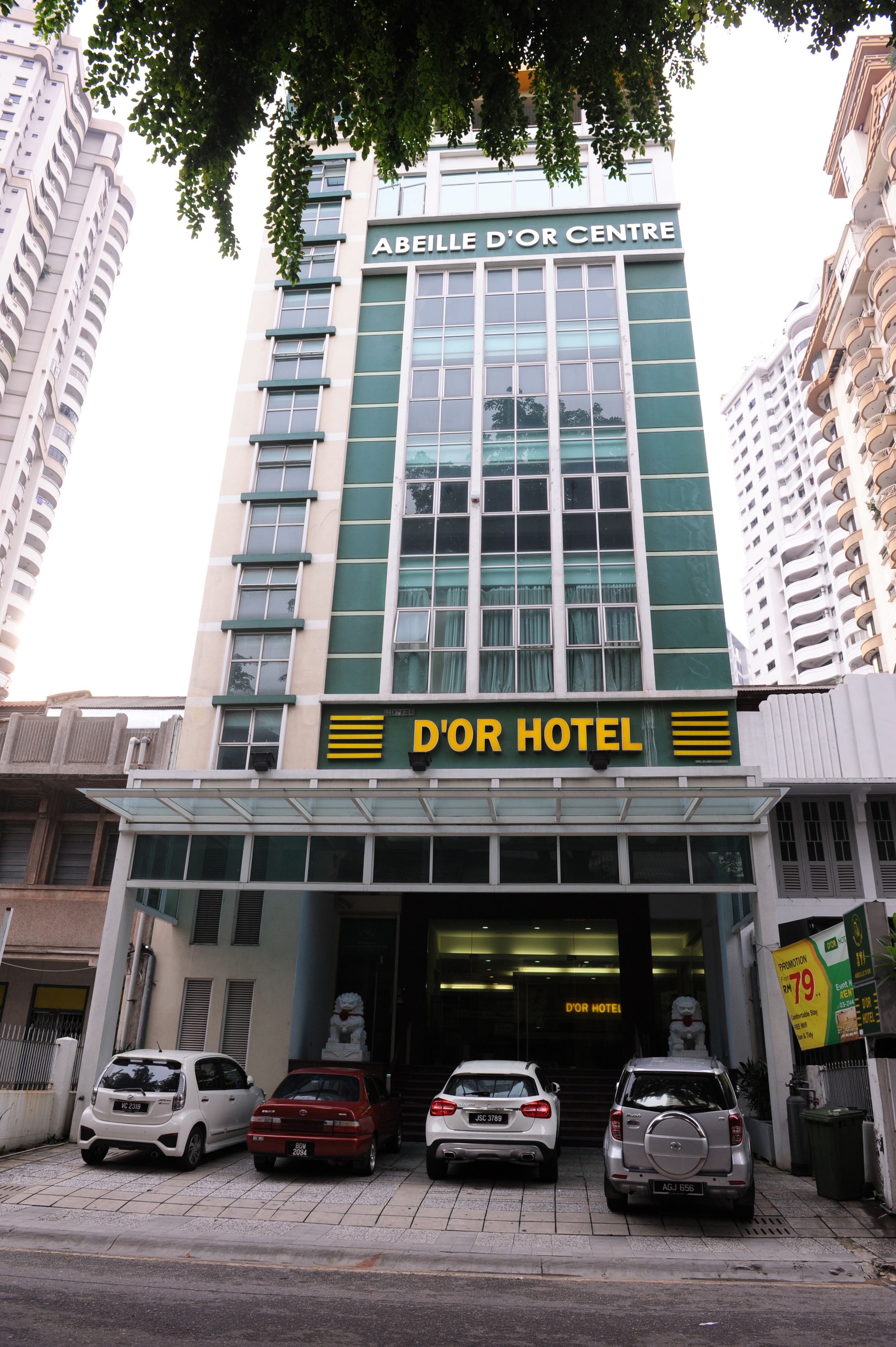 Un hôtel avec une enseigne bien visible indiquant « HÔTEL D’OR » et « ABEILLE D’OR CENTRE ». Trois voitures sont garées devant.
