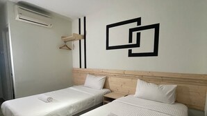 Ein Hotelzimmer mit zwei Betten, einem Holzkopfteil, einer Wand-Klimaanlage und einer schlichten geometrischen Wanddekoration.