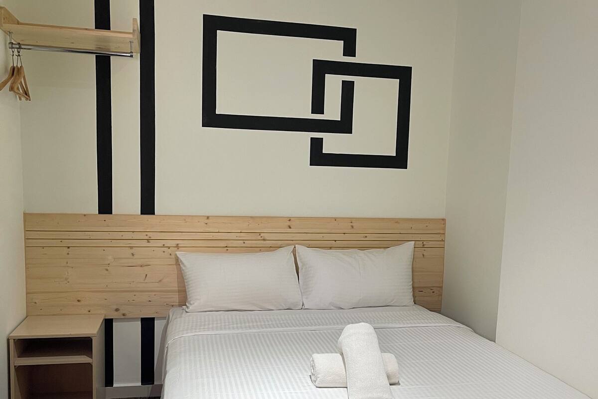 A hotel room with a wooden headboard, a bed with white linens, a wall art piece, and a small bedside table.