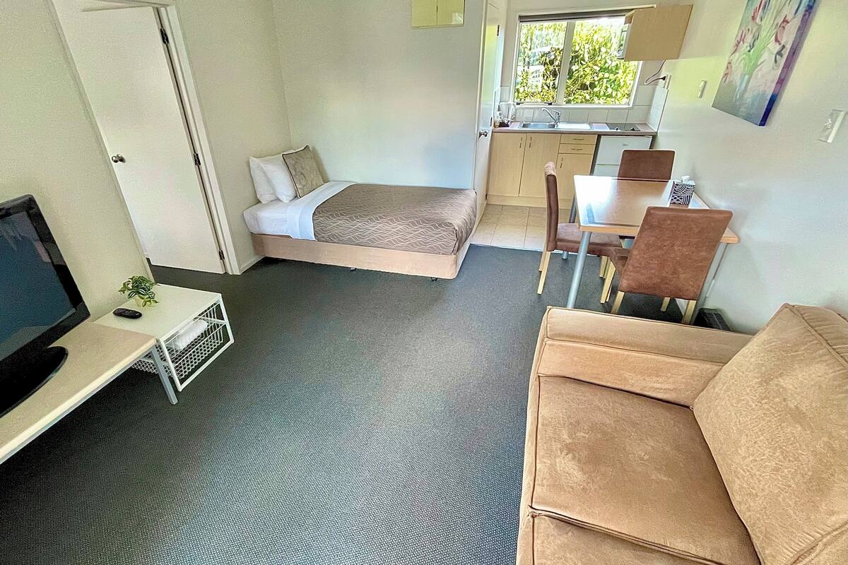 Una habitación compacta con cama, escritorio, silla y una pequeña kitchenette.