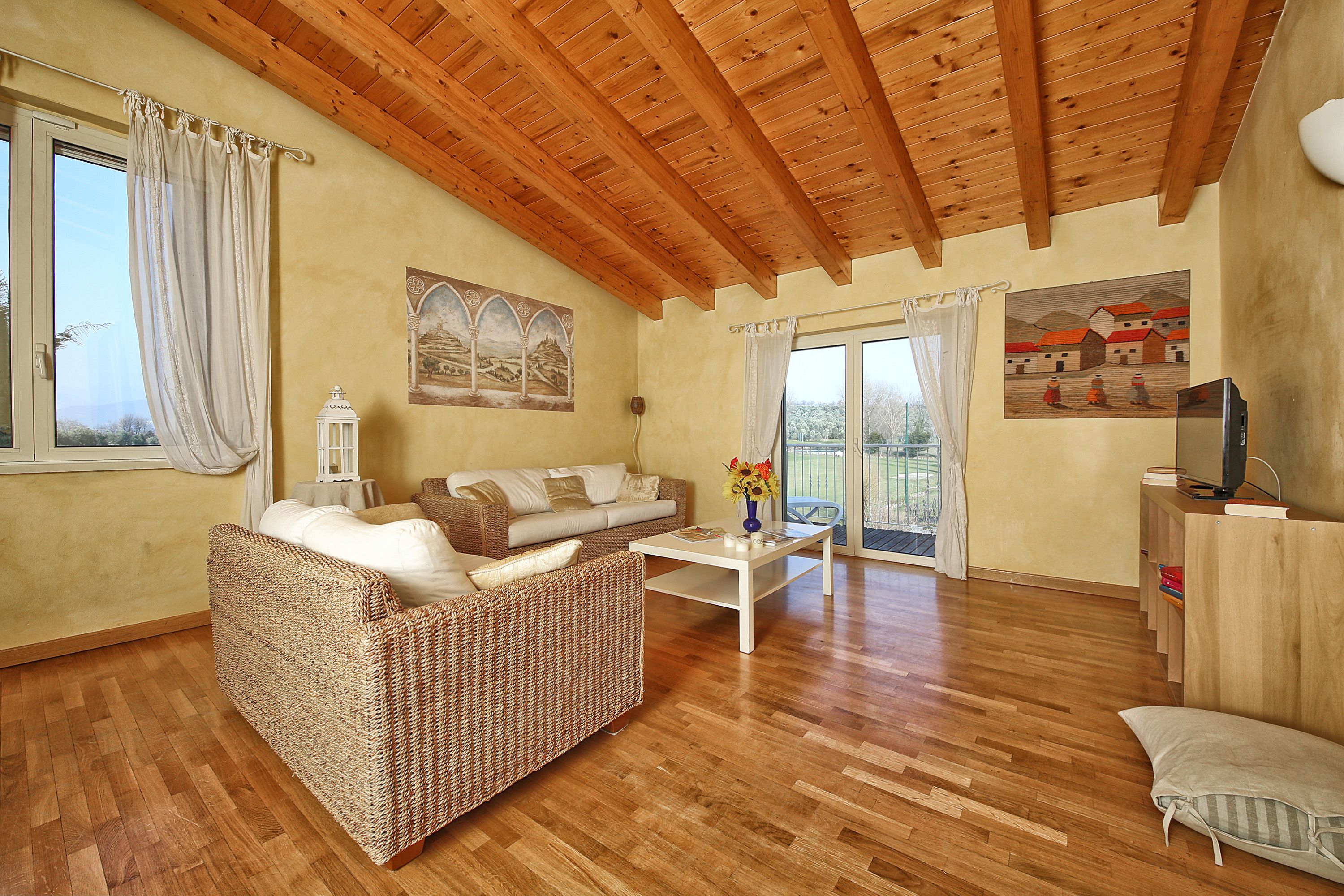 Un accogliente soggiorno con soffitto in legno, un divano, un tavolino e una televisione.