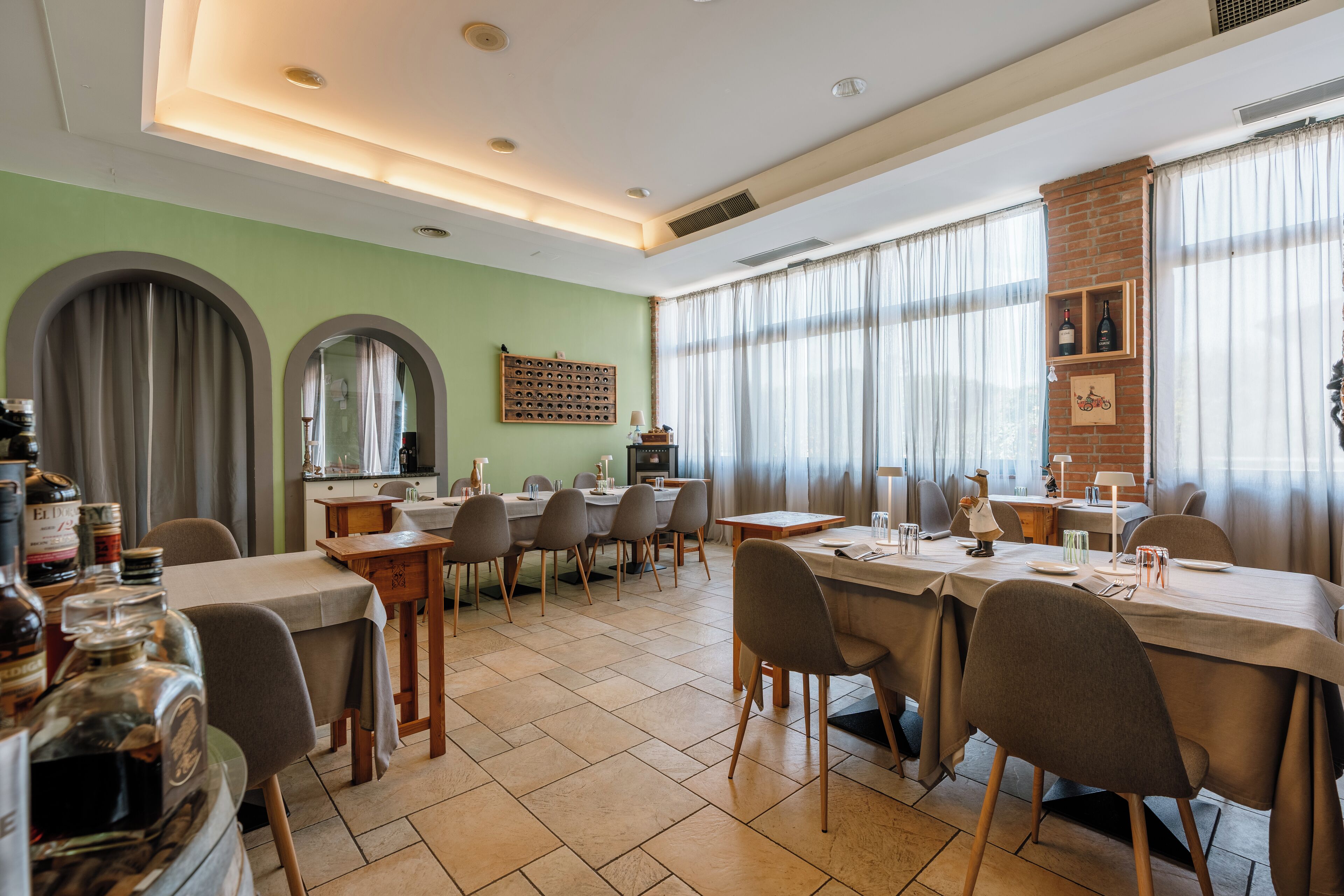 A dining area with multiple tables and chairs, a brick wall, and large windows with curtains.