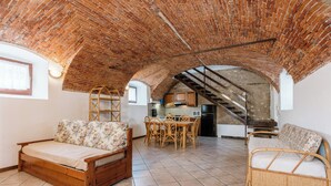 Ein geräumiges Loft mit hoher, freiliegender Backsteinwand, einem Essbereich mit Holzmöbeln und einer Treppe zu einer erhöhten Ebene.