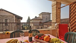 Ein Balkon mit einem Tisch, der für eine Mahlzeit gedeckt ist, mit einer Weinflasche, einer Obstschale und einer karierten Tischdecke.