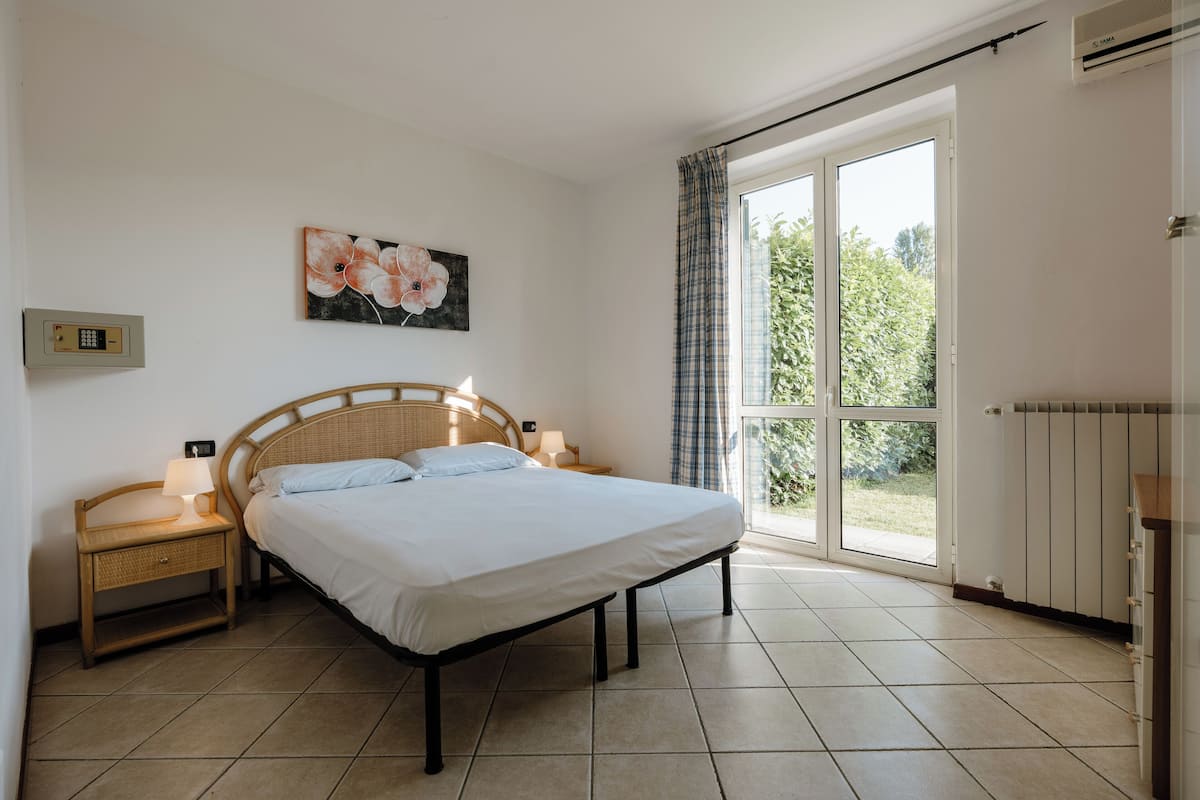 Ein Schlafzimmer mit einem Bett, Nachttischen, einer Wandleuchte, einem Fenster mit Vorhängen und einer Heizung.