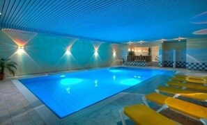 Una piscina interior con suelo de baldosas, sillones de descanso amarillos y una zona de bar con suelo de estampado a cuadros.