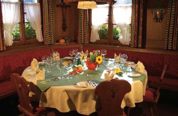 Comedor con una mesa redonda dispuesta para seis comensales, cubierta con mantel verde y rodeada de sillas tapizadas rojas.